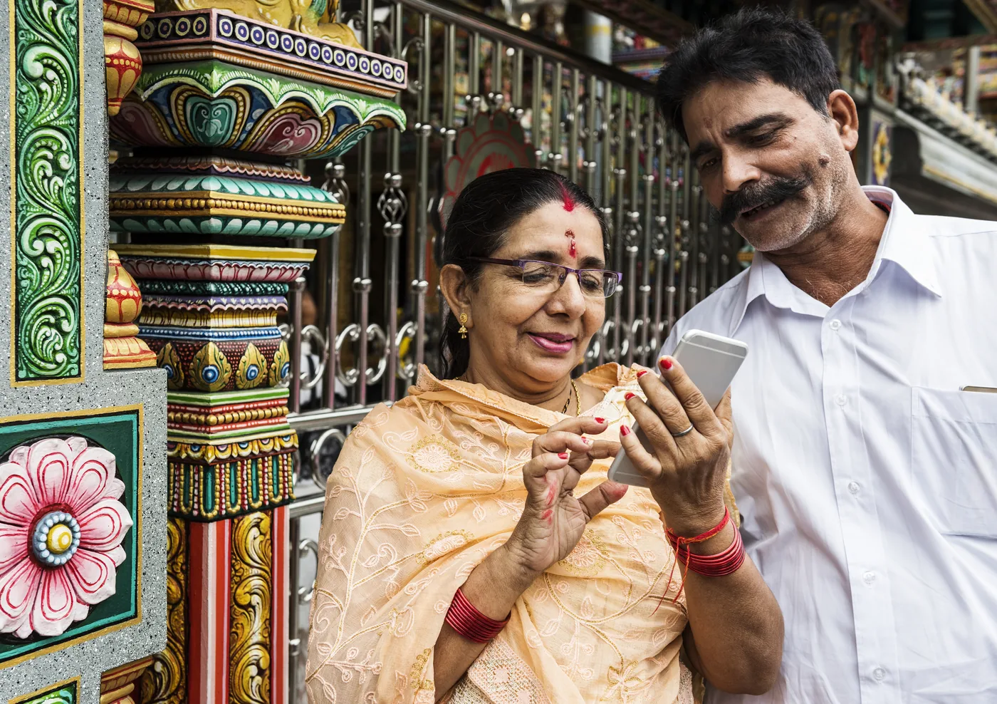 Visitors using a mobile phone outside an ornate Hindu temple